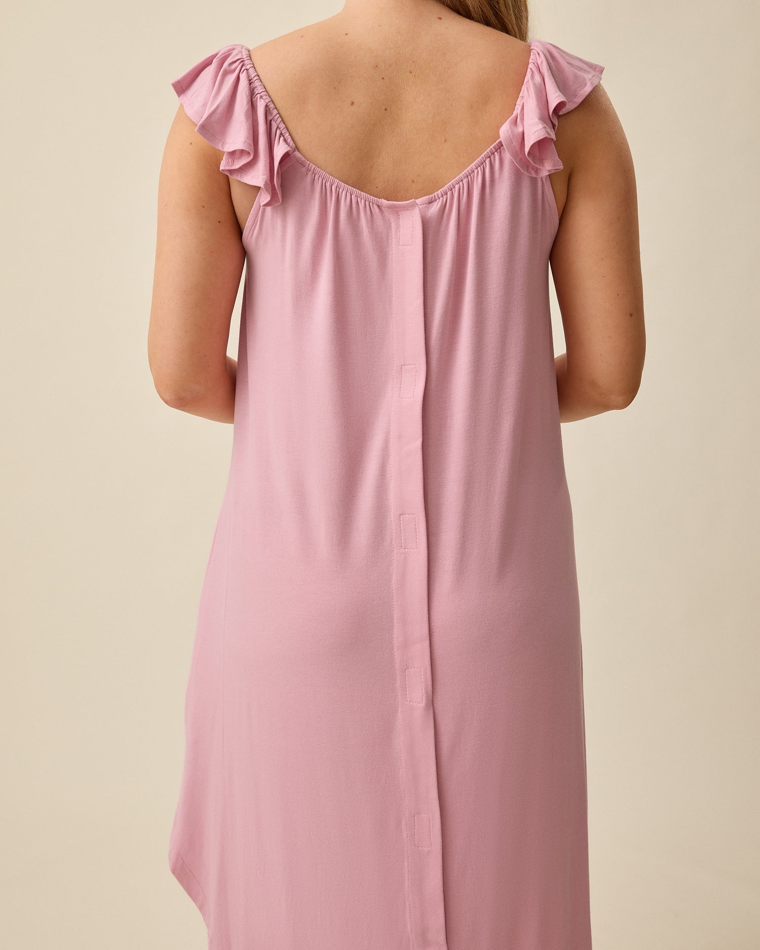 Back view of model wearing Ruffle Strap Labor & Delivery Gown in Light Mauve on a beige background