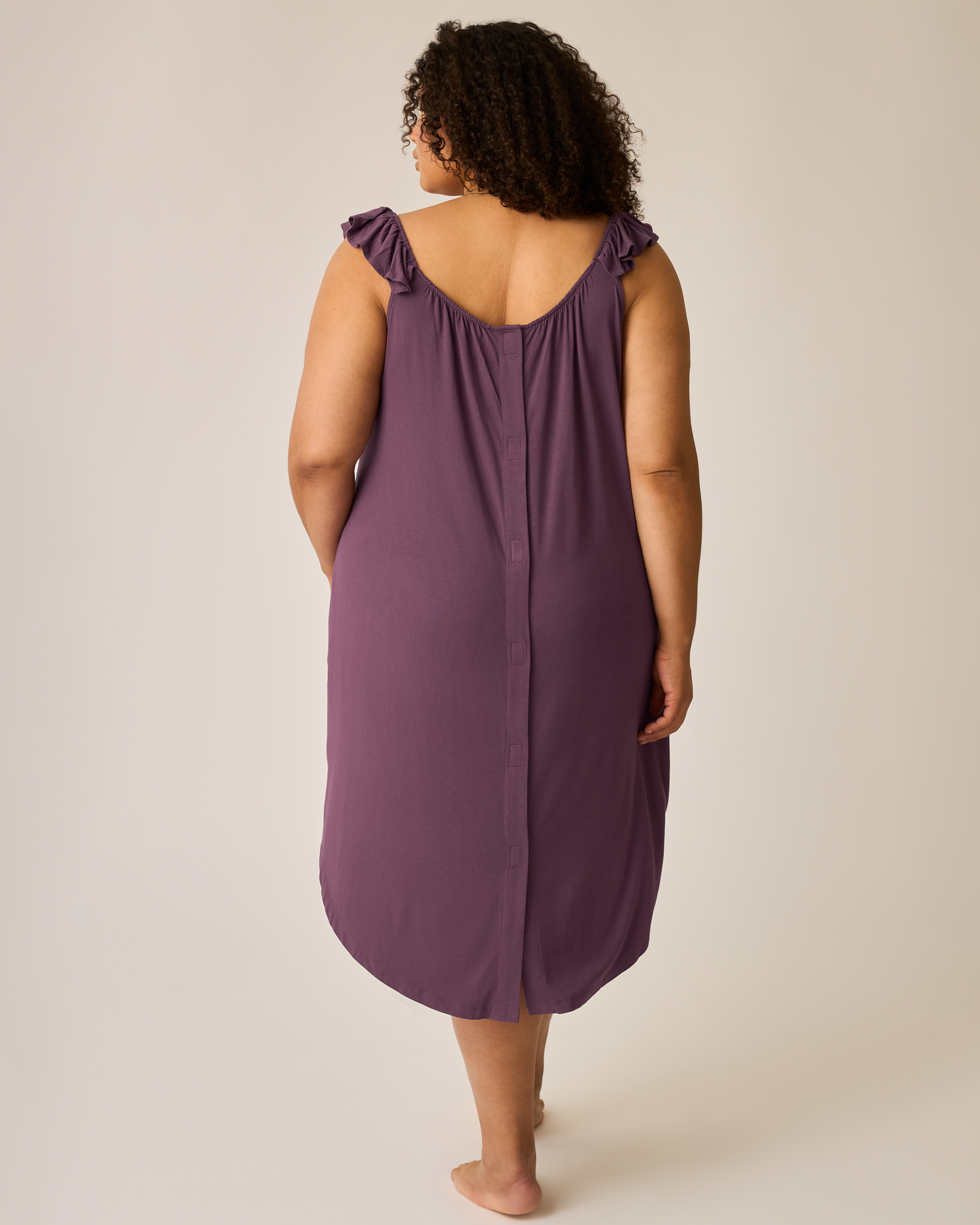 Person wearing a purple labor & delivery gown with ruffled straps on a plain background
