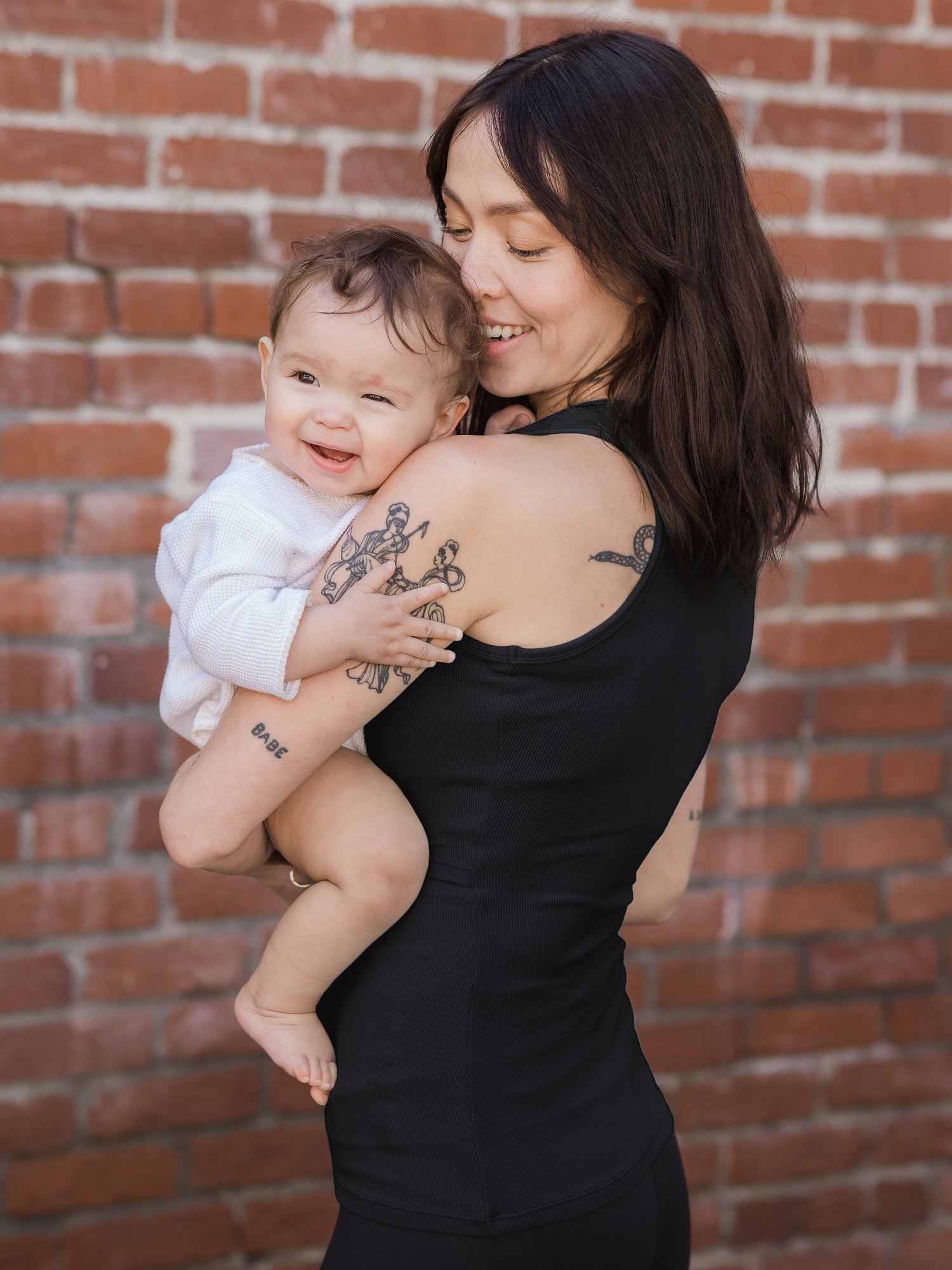 Side view of model holding baby and wearing the Ribbed Bamboo Racerback Nursing Tank in black 