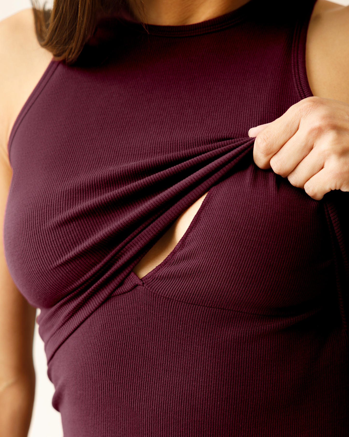 Cropped in view of woman wearing the Ribbed Bamboo Racerback Nursing Tank in Deep Burgundy, lifting up top outer layer to show nursing access.