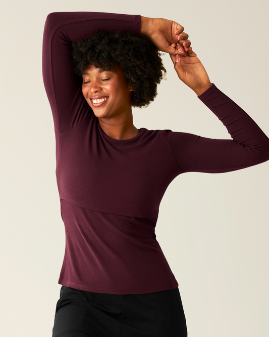 Woman wearing the Ribbed Bamboo Long Sleeve Nursing T-shirt in Deep Burgundy on beige background @model_info:Kyra is wearing a Small.