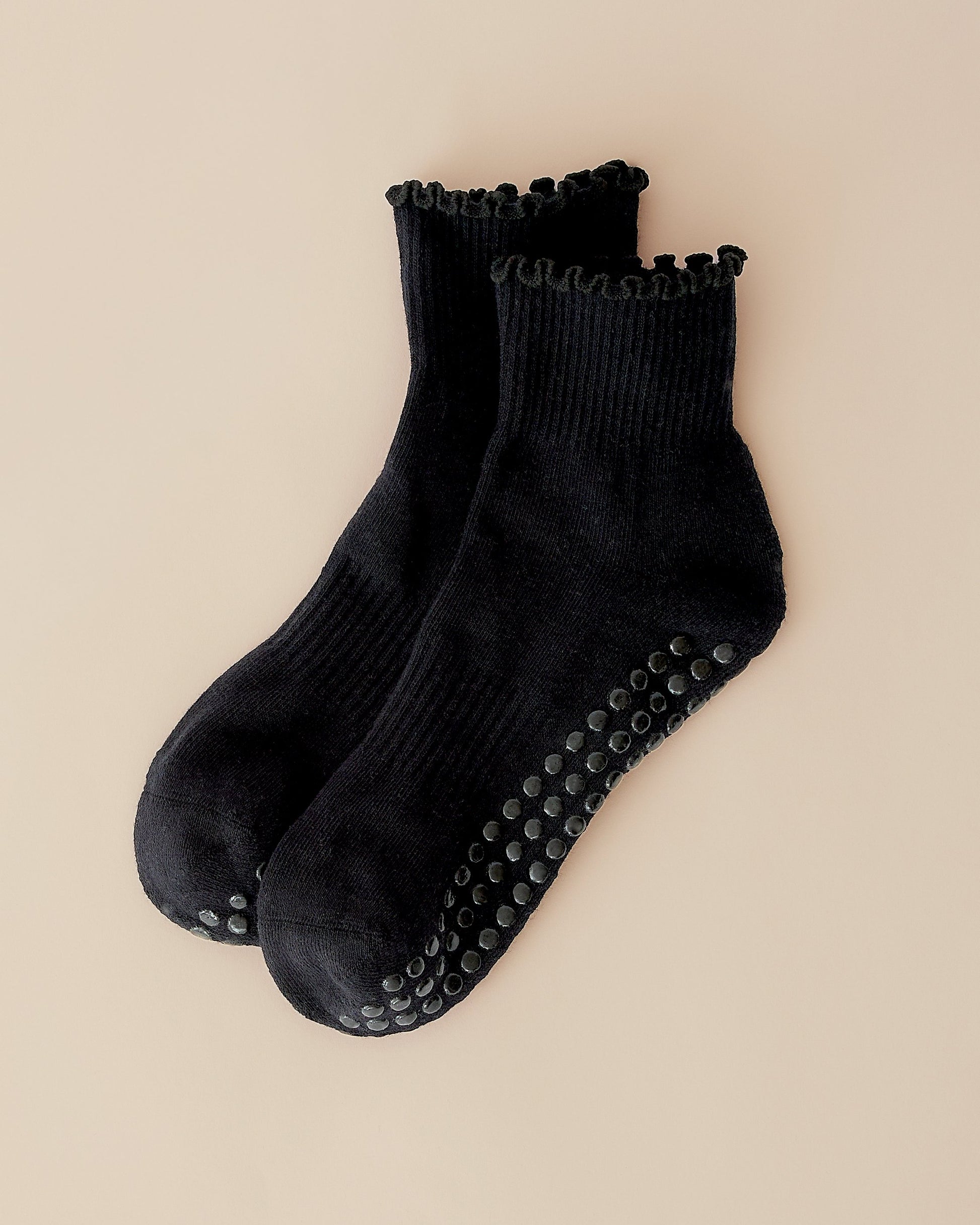A pair of Non-Slip Ruffle Ankle Socks in Black on a beige background.
