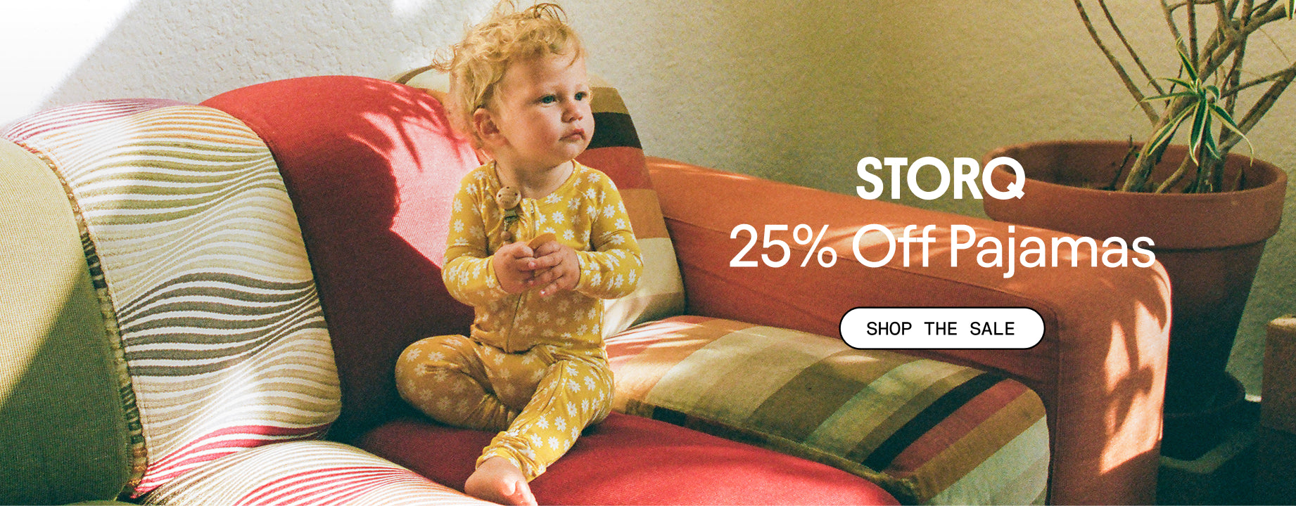 White text over image: STORQ 25% Off Pajamas. White button: Shop the Sale. Photo of baby in Bamboo Baby Pajama in Yellow Daisies on a patterned couch. 