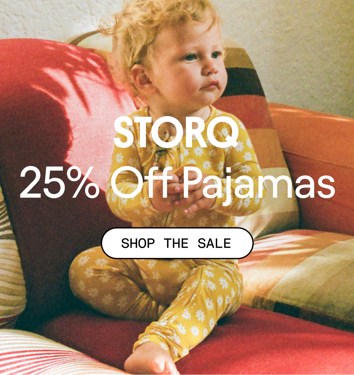 White text over image: STORQ 25% Off Pajamas. White button: Shop the Sale. Photo of baby in Bamboo Baby Pajama in Yellow Daisies on a patterned couch. 