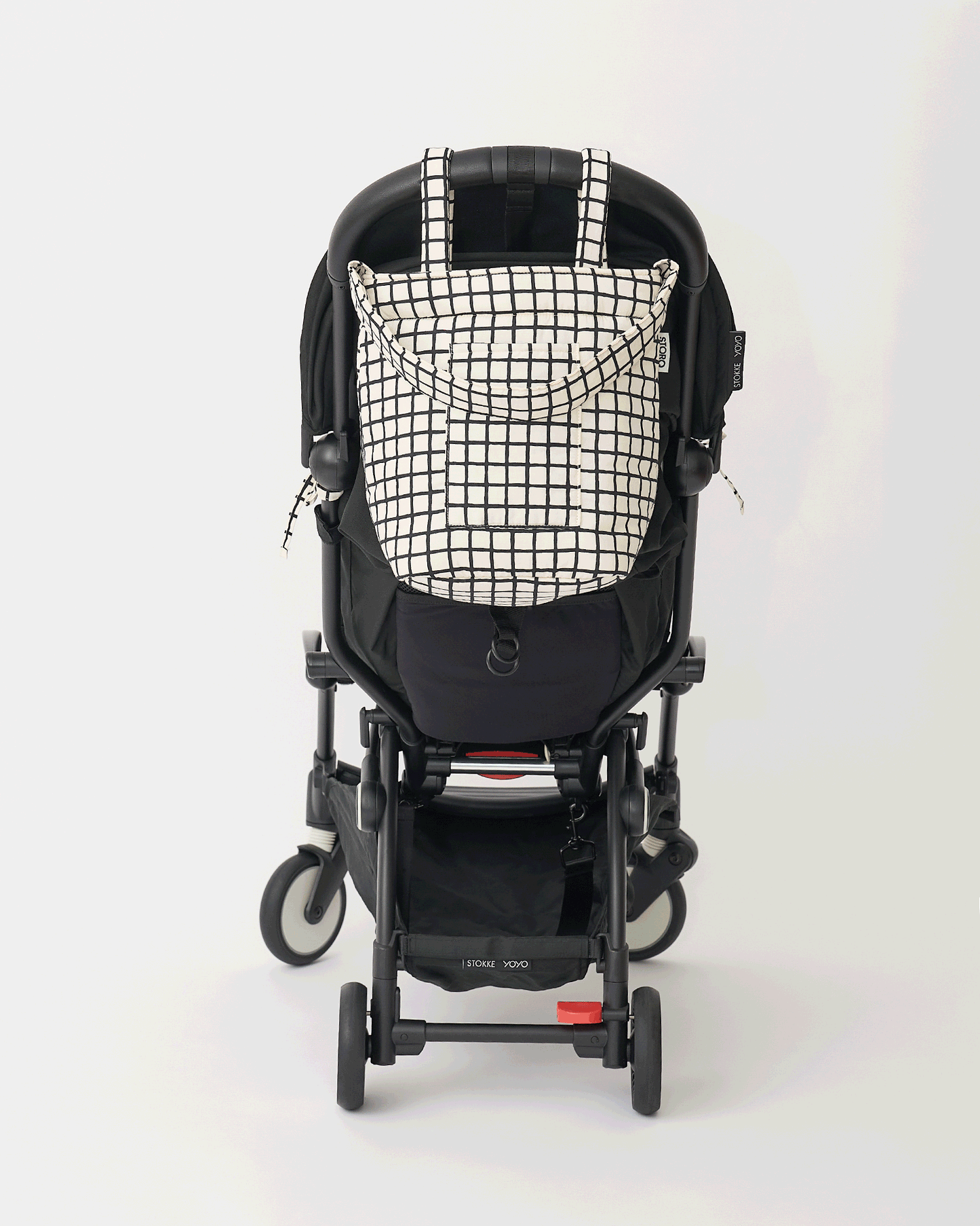 Animated Gif of black stroller rotating with Stroller Party™ Seat Liner & Strap Covers in Black Grid, and Stroller Party™ Bucket Bag in Black Grid hanging off the handlebars, on an off white background.