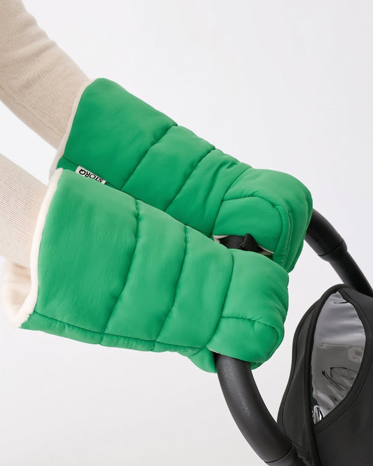 Model is wearing Cozy Stroller Mitts in Green while pushing a black stroller handlebar on an off white background.