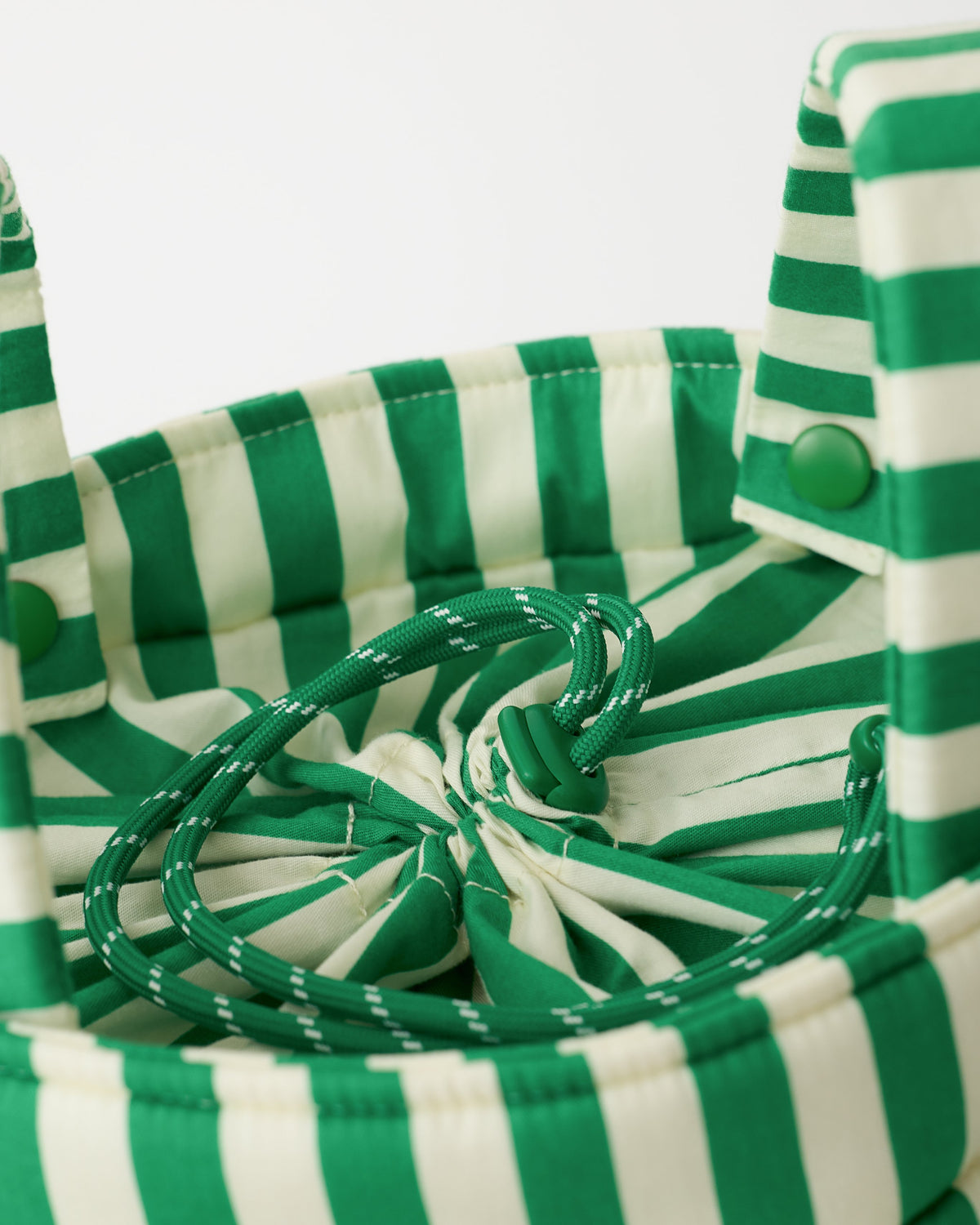 Close up of Stroller Party™ Bucket Bag top in Green Stripe, with drawstring pulled tightly shut, on a beige background.