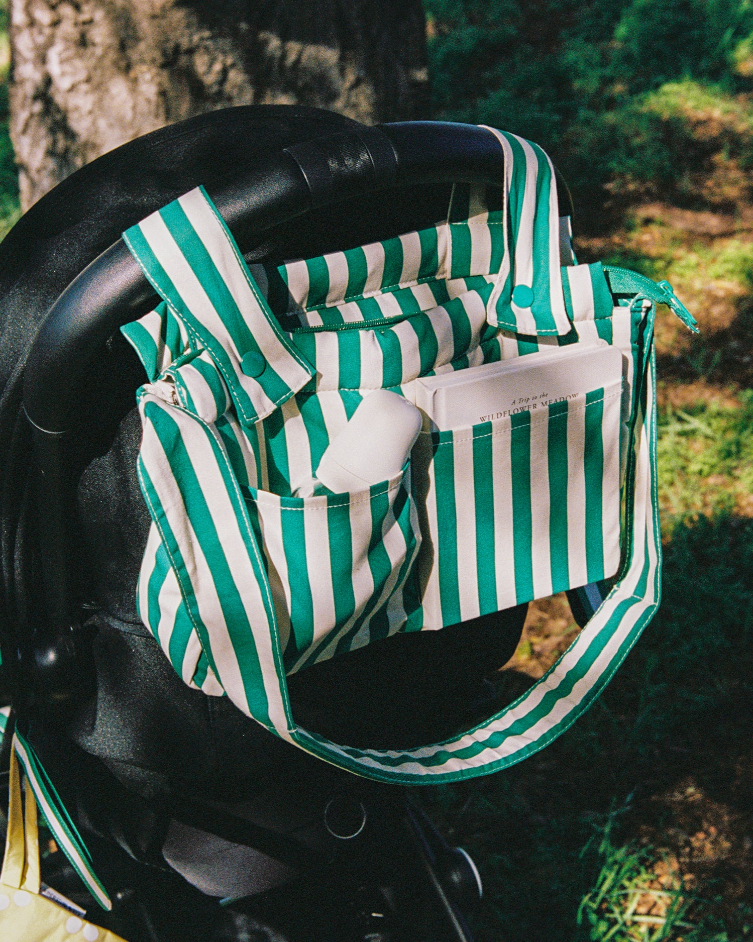 Stroller Party Caddy Bag in Green Stripe, placed on a stroller's handle, outside
