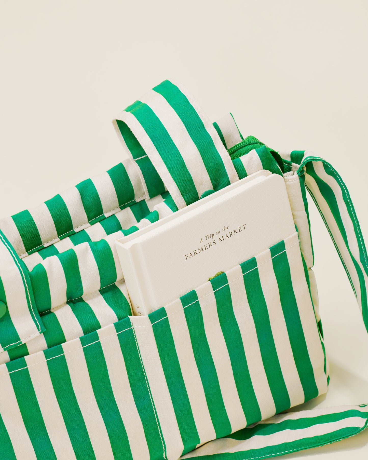 Close up of Stroller Party Caddy Bag in Green Stripe, with a notebook placed on the outside pocket of the bag