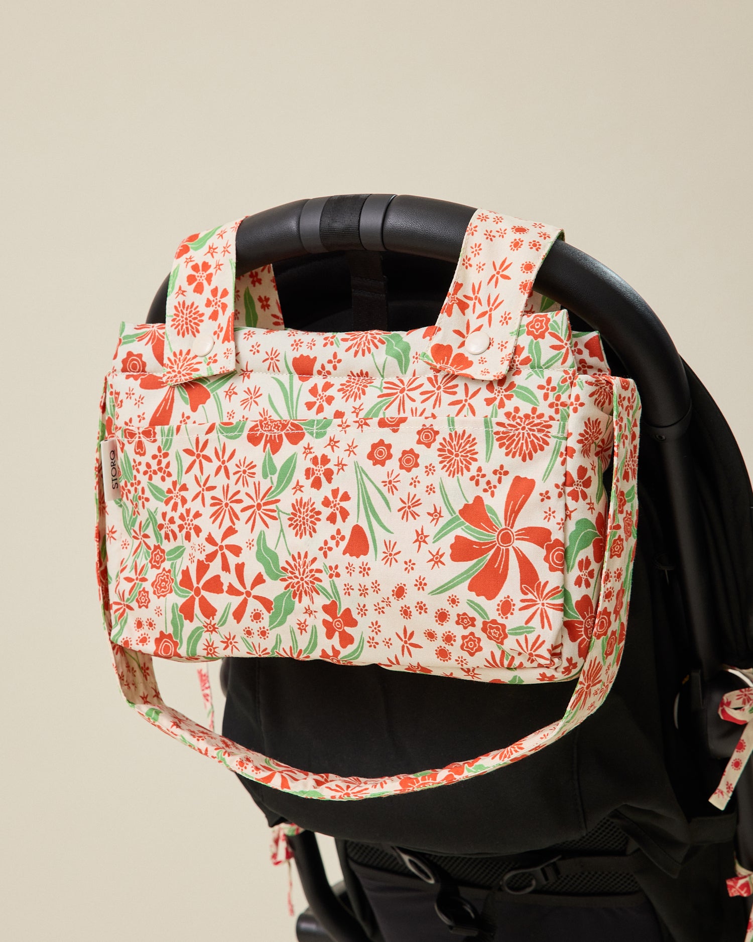 Stroller Party Caddy Bag in Superbloom hanging from handlebar of black stroller on a beige background