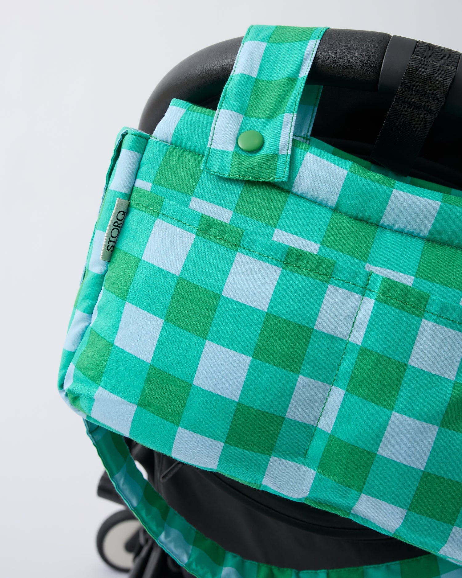 Black Stroller with Stroller Party™ Caddy Bag in Teal Gingham clipped onto the handle bar, on a beige background.