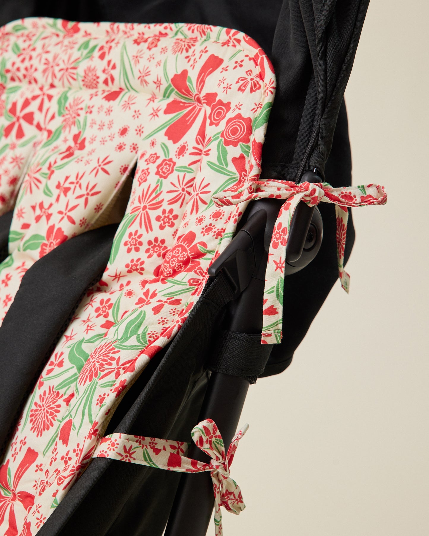 Close up of Stroller Party Seat Liner in Superbloom set in stroller seat to display how ties easily wrap around stroller to secure liner into seat, on a beige background