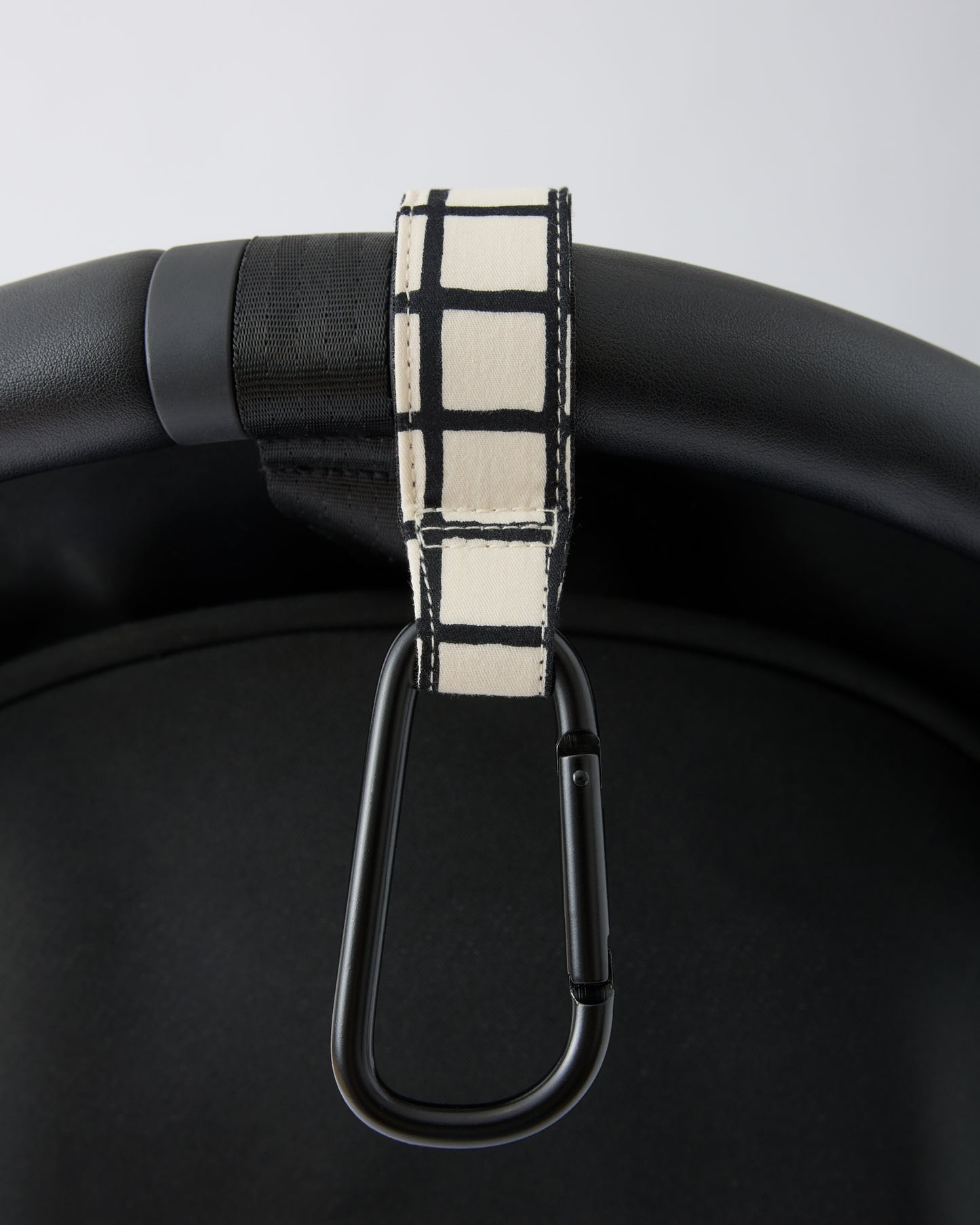 Black stroller handle bar with Stroller Party™ Clips (2-Pack) in Black Grid attached, on a beige background.