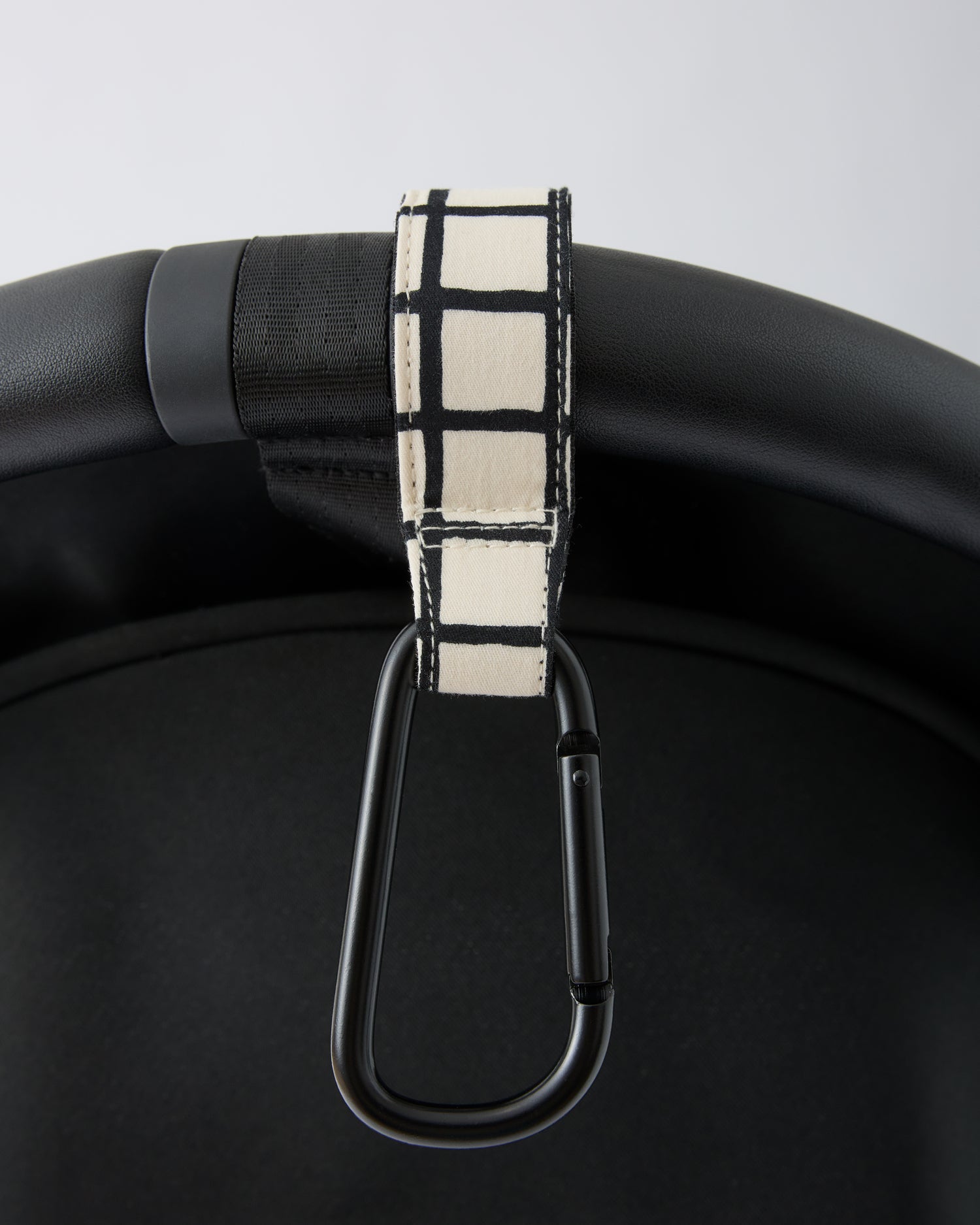 Black stroller handle bar with Stroller Party™ Clips (2-Pack) in Black Grid attached, on a beige background.