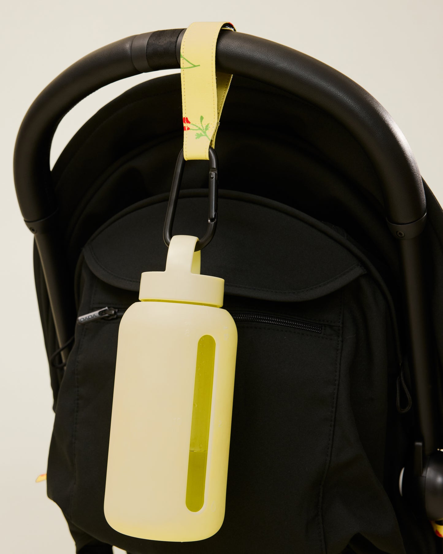 Stroller Party Clips in Sunshine Wildflower attached to a stroller's handle and holding a bottle