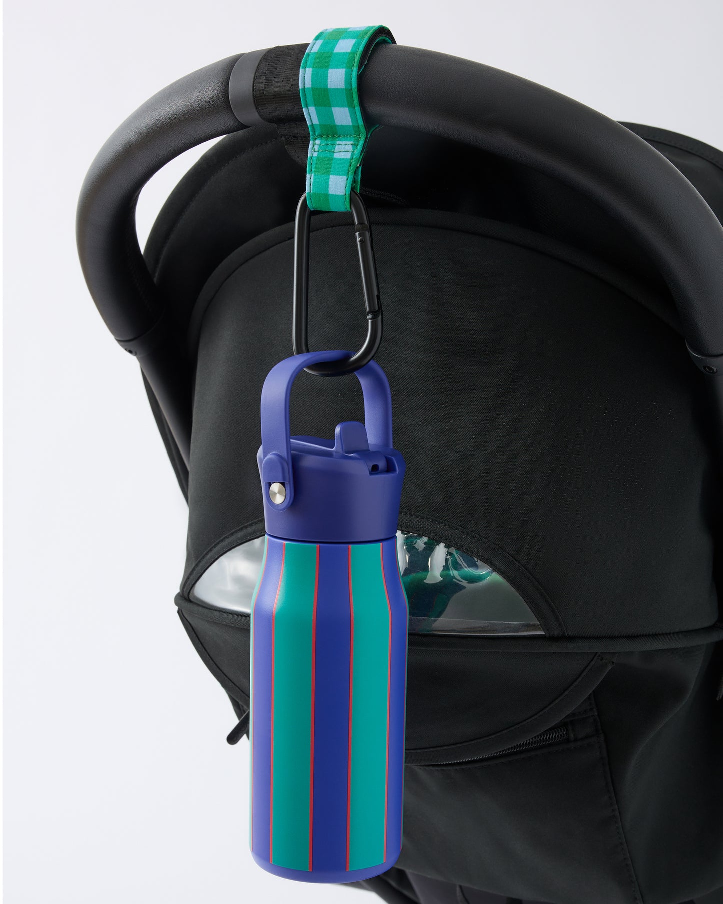 Black stroller handle bar with Stroller Party™ Clips (2-Pack) in Teal Gingham attached, while holding a Cool Kid Water Bottle in Navy & Green Stripe on a beige background.
