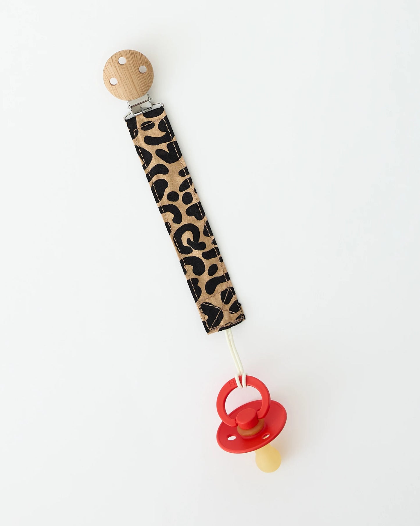 Close up of Pacifier Clip in Leopard, holding onto a red pacifier, on a beige background.