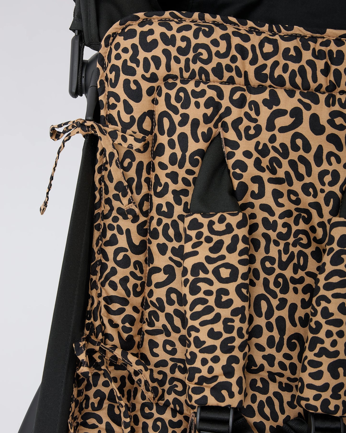 Close up of the ties that connect Stroller Party™ Seat Liner & Strap Covers in Leopard to the frame of a black stroller, on a beige background.