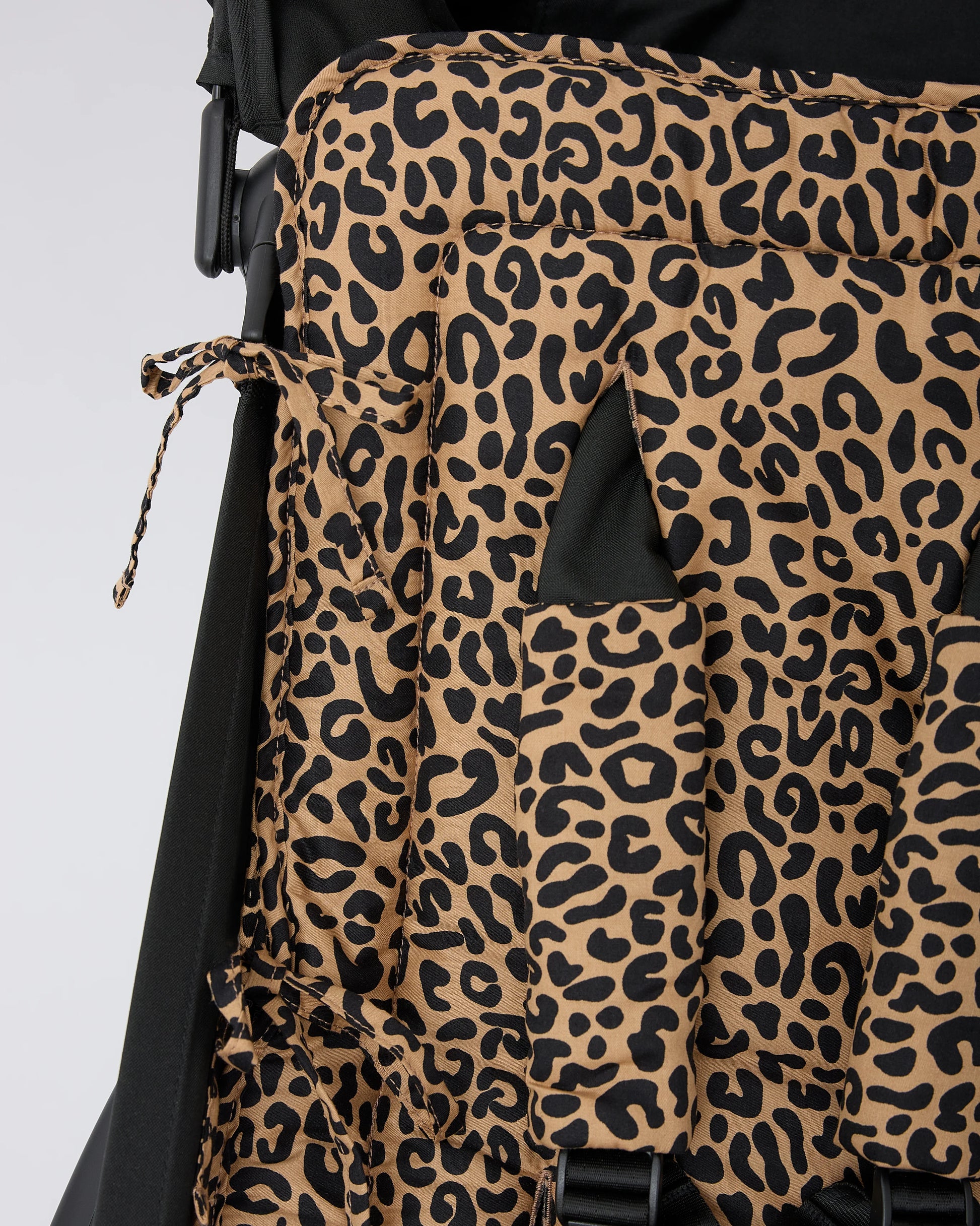 Close up of the ties that connect Stroller Party™ Seat Liner & Strap Covers in Leopard to the frame of a black stroller, on a beige background.