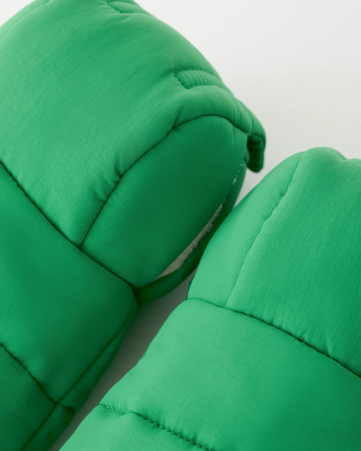 Close up of the exterior of the Cozy Stroller Mitts in Green on an off white background.