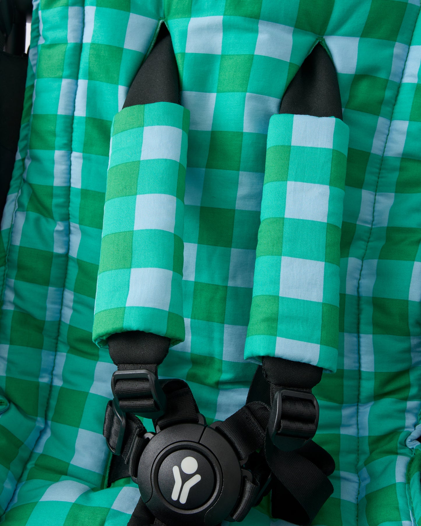 Close up of black stroller with Stroller Party™ Seat Liner & Strap Covers in Teal Gingham on a beige background.
