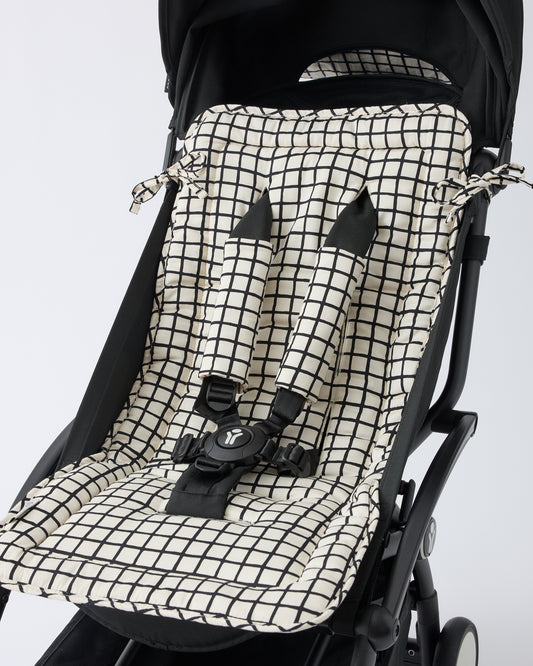 Black stroller with Stroller Party™ Seat Liner & Strap Covers in Black Grid on a beige background.