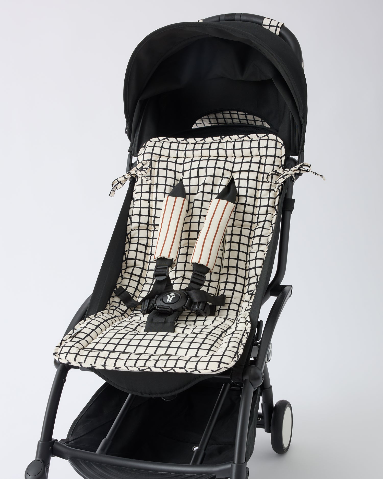 Black stroller with Stroller Party™ Seat Liner & Strap Covers in Black Grid on a beige background. Straps are reversed for new pattern.
