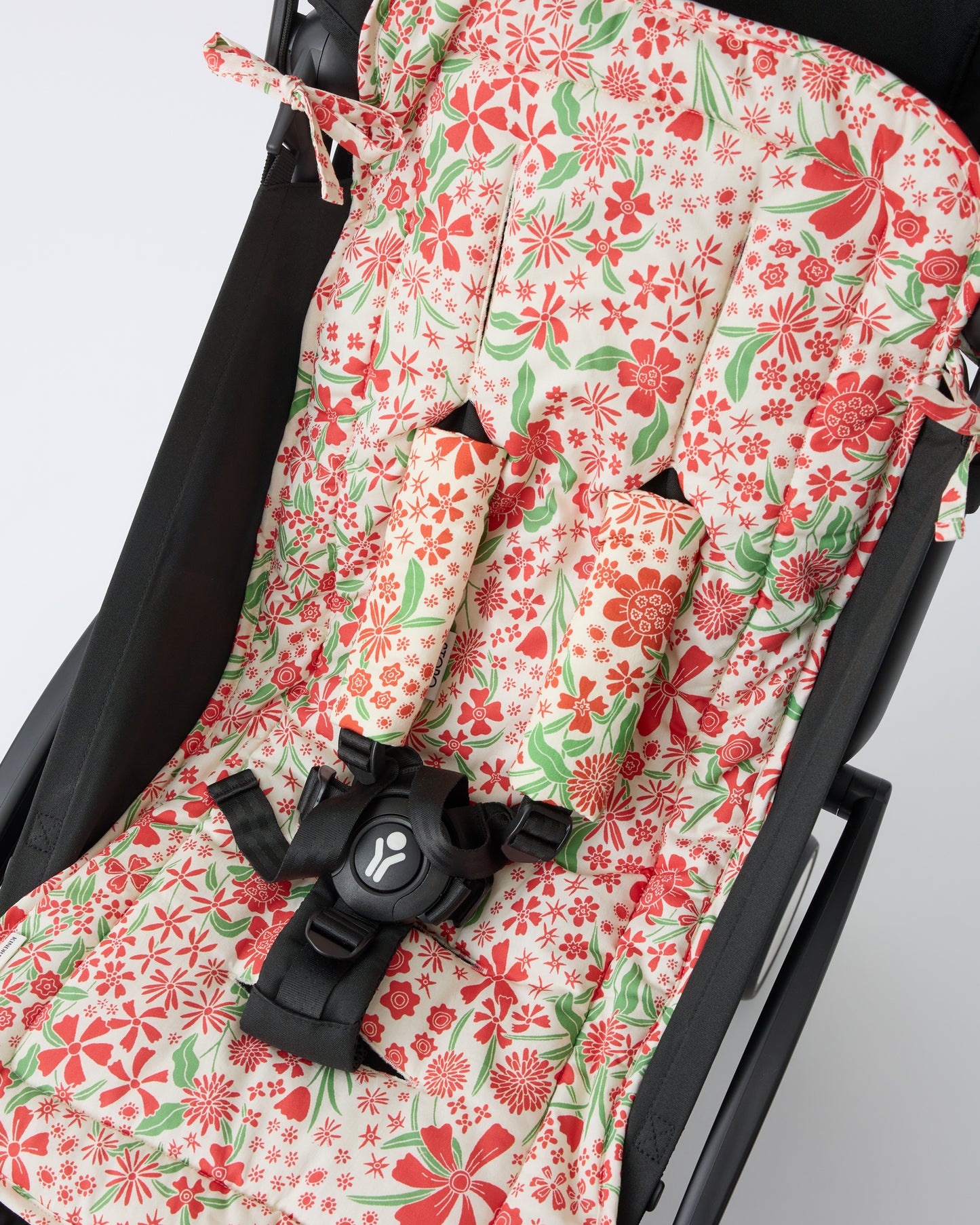 Black stroller with Stroller Party™ Seat Liner & Strap Covers in Superbloom on a beige background.