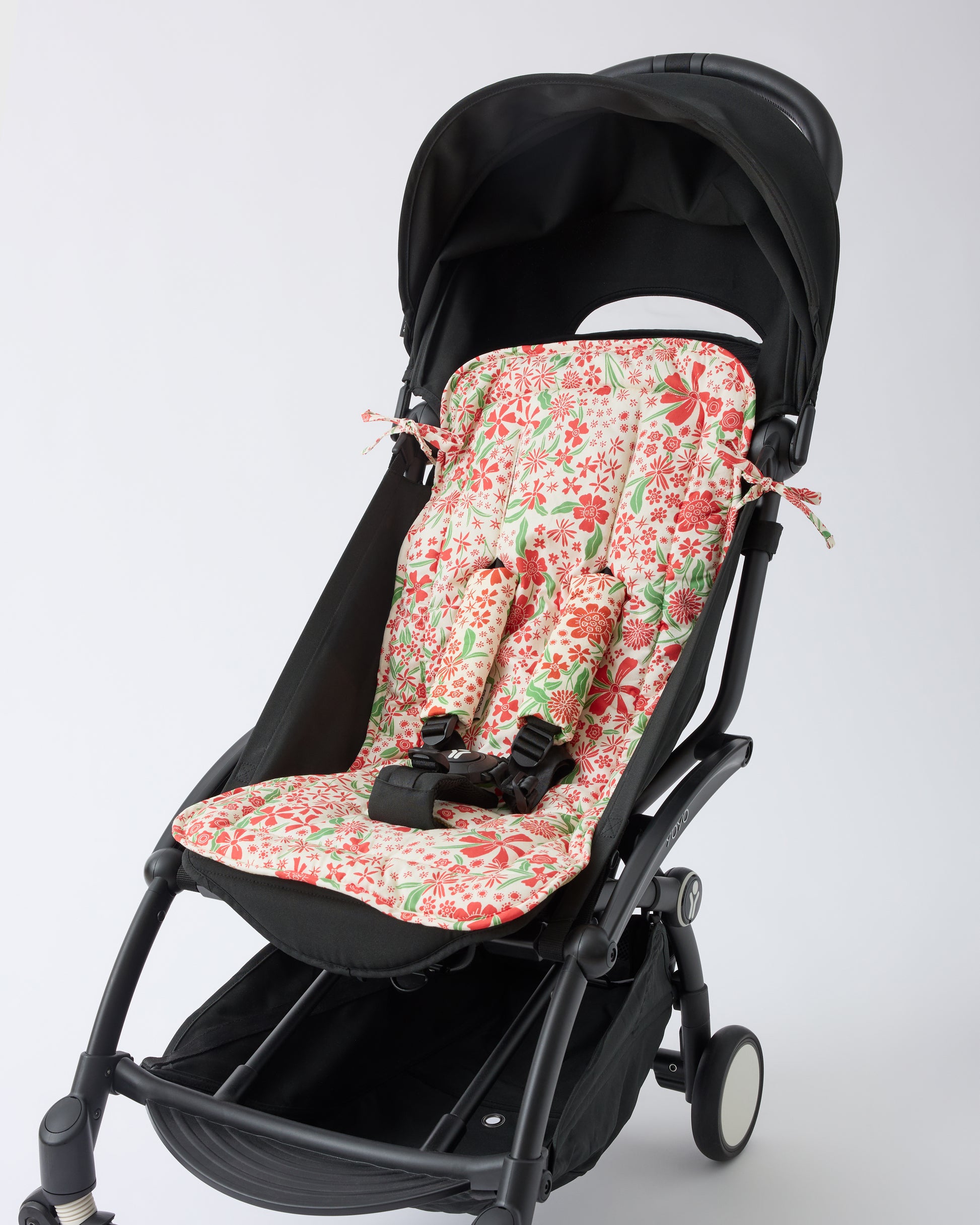 Black stroller with Stroller Party™ Seat Liner & Strap Covers in Superbloom on a beige background.