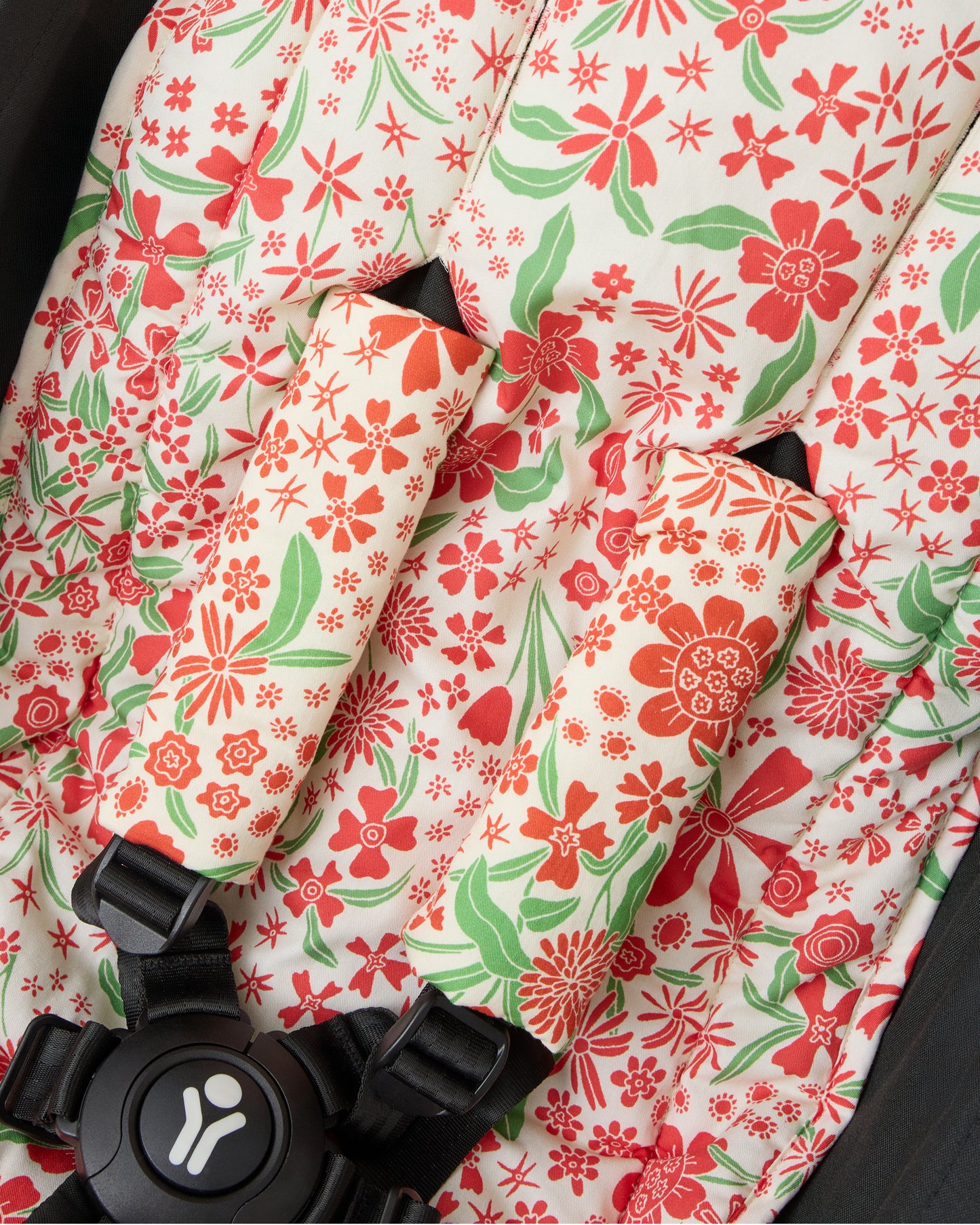 Close up of black stroller with Stroller Party™ Seat Liner & Strap Covers in Superbloom on a beige background.