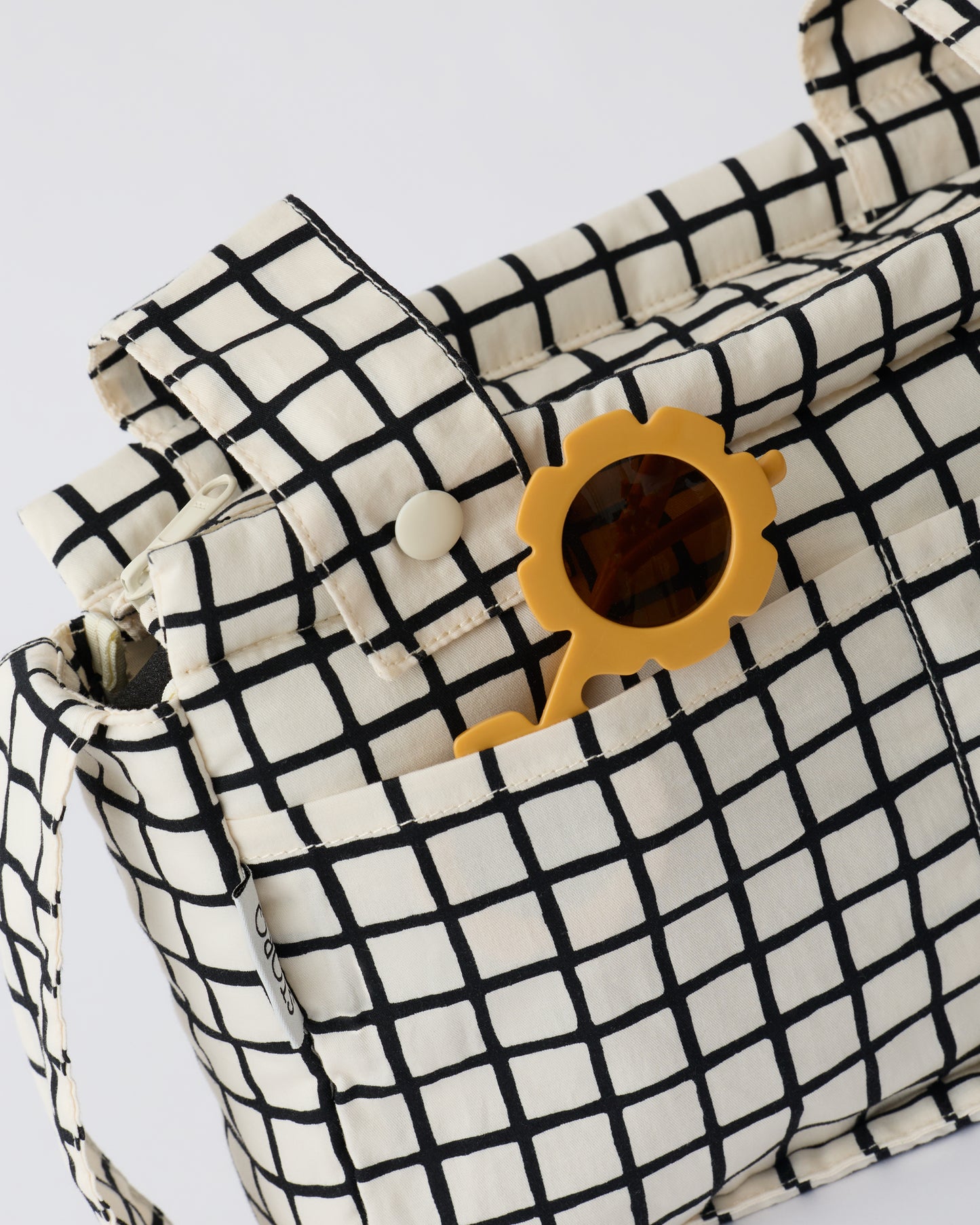 Stroller Party™ Caddy Bag in Black Grid, with sunglasses sticking out of outer pocket, on a beige background.