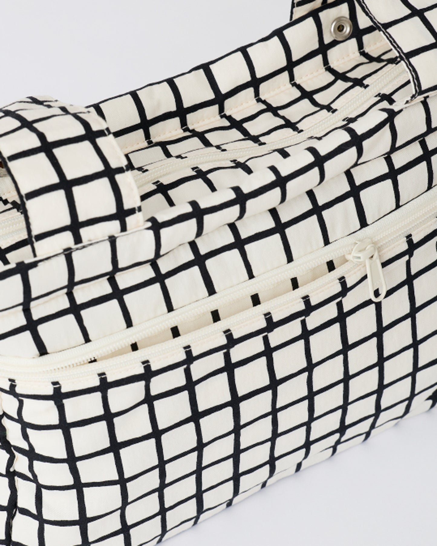 Close up of the pockets of the Stroller Party™ Caddy Bag in Black Grid, on a beige background.