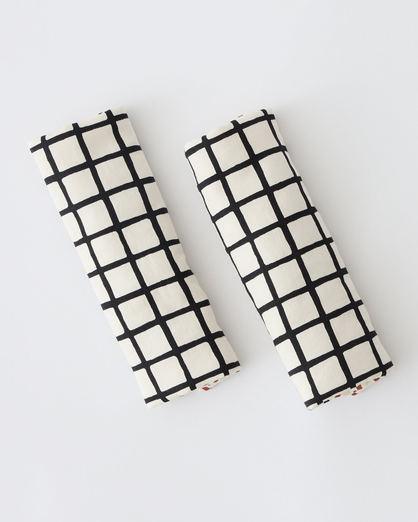 Folded Stroller Party™ Strap Covers in Black Grid on a beige background. 