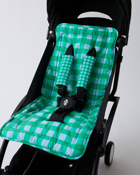 Black stroller with Stroller Party™ Seat Liner & Strap Covers in Teal Gingham on a beige background.