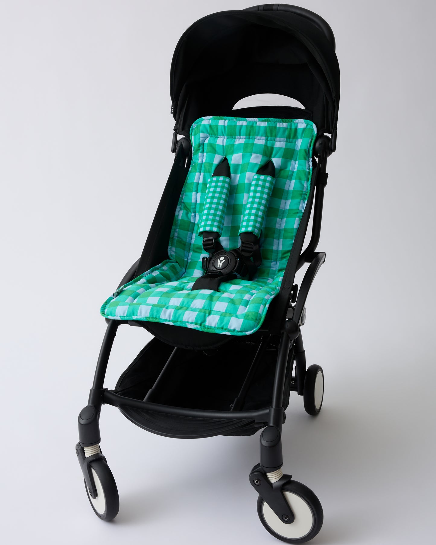 Black stroller with Stroller Party™ Seat Liner & Strap Covers in Teal Gingham on a beige background.