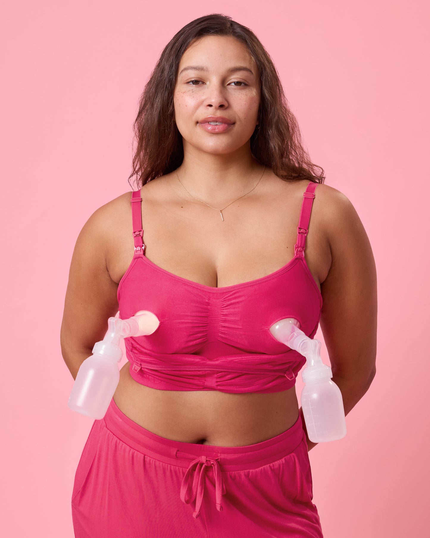 Front view of model wearing Sublime Hands-Free Pumping & Nursing Bra  Raspberry Pink on a pink background with a pump attached