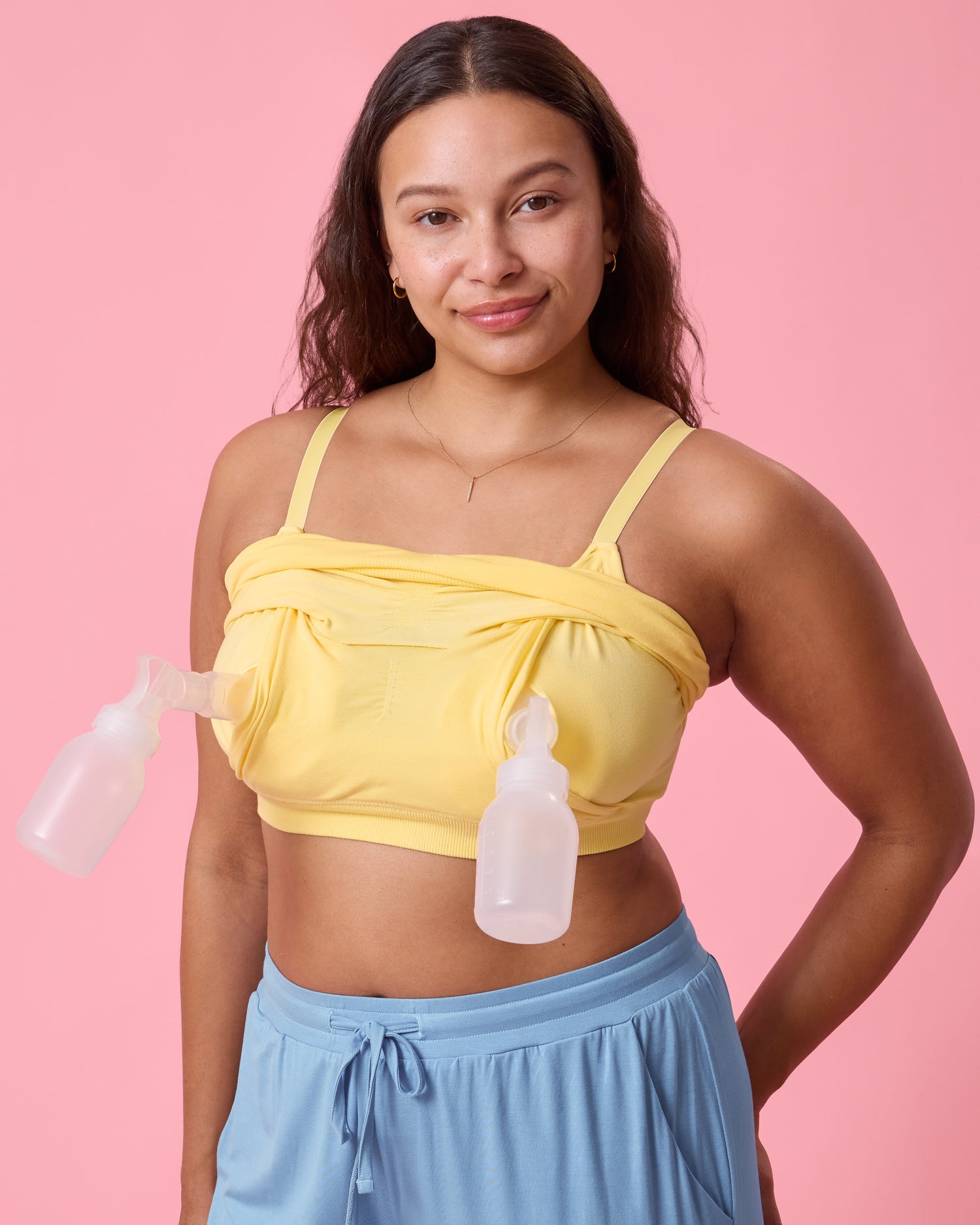 Front view of model wearing Sublime Bamboo Hands-Free Pumping Lounge & Sleep Bra in Dandelion on a pink background while pumping