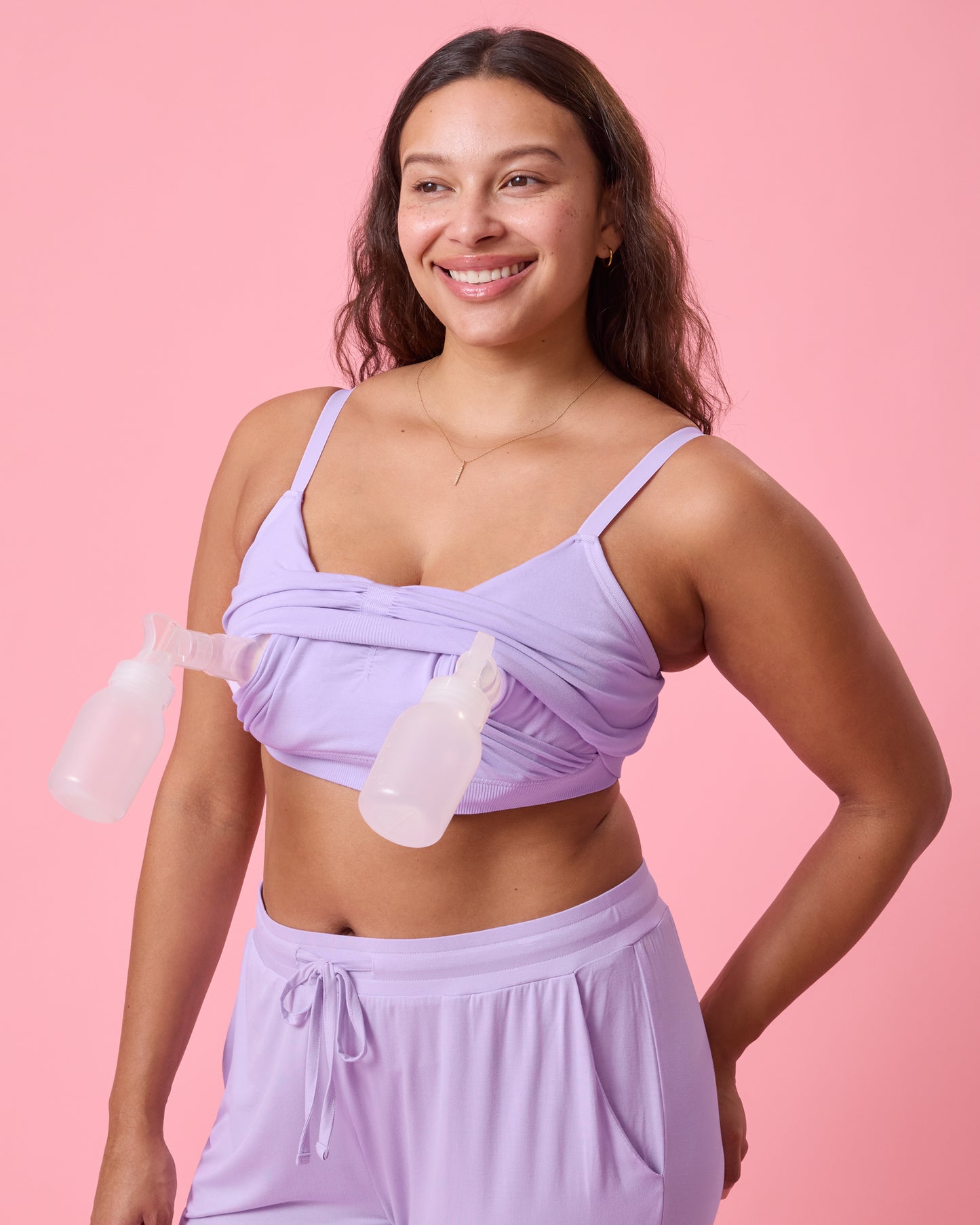 Front view of model wearing Sublime Bamboo Hands-Free Pumping Lounge & Sleep Bra in Lavender on a pink background while pumping