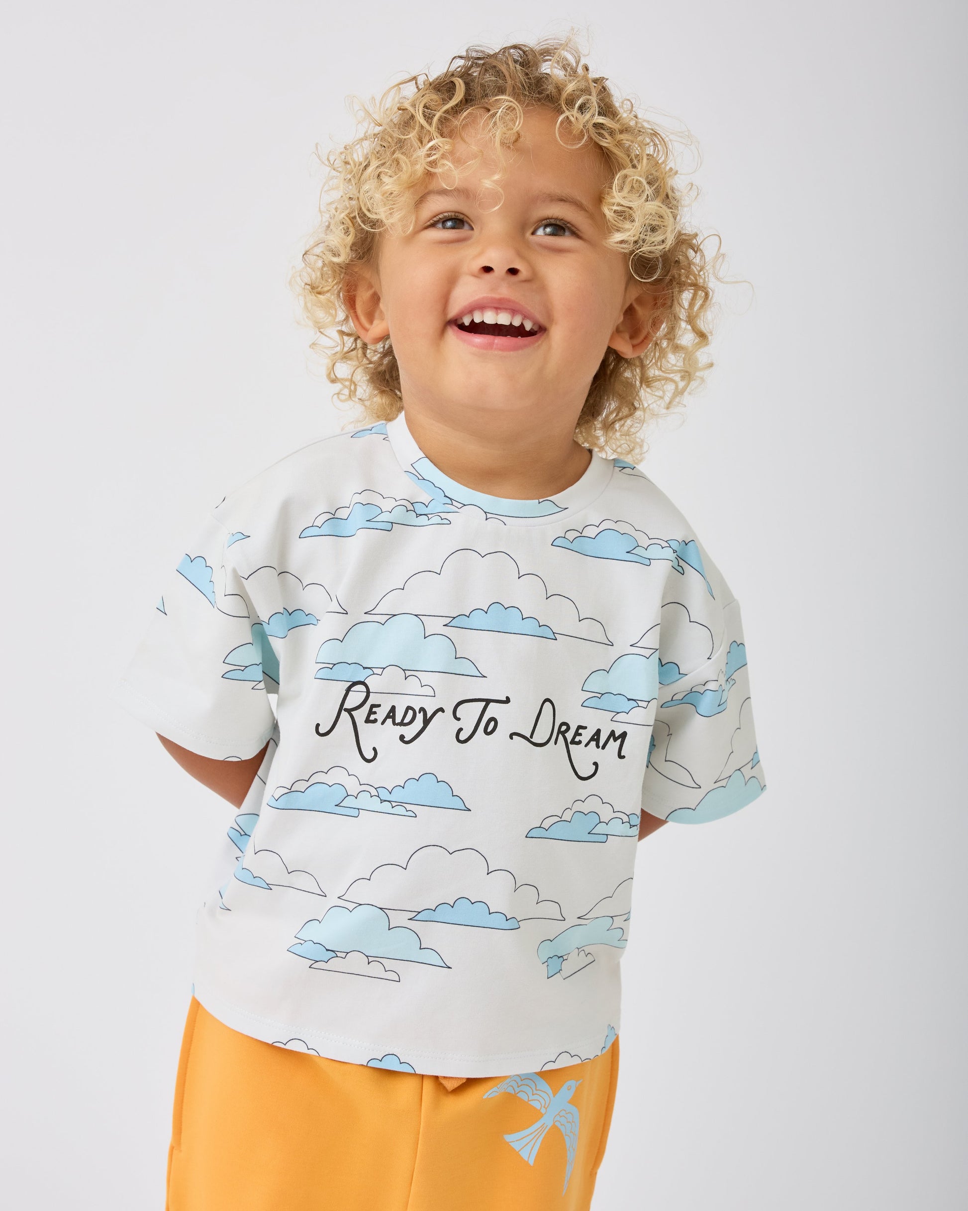 Model is wearing Graphic Tee in Ivory Clouds and French Terry Jogger in Orange Bird on a gray background.@model_info:Waylon is 3 years old and wearing 3T.