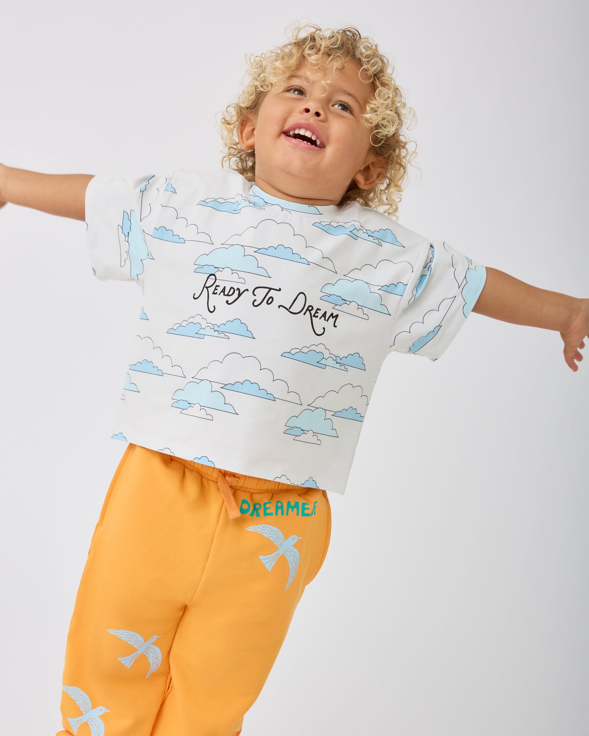 Model is wearing Graphic Tee in Ivory Clouds and French Terry Jogger in Orange Bird on a gray background.