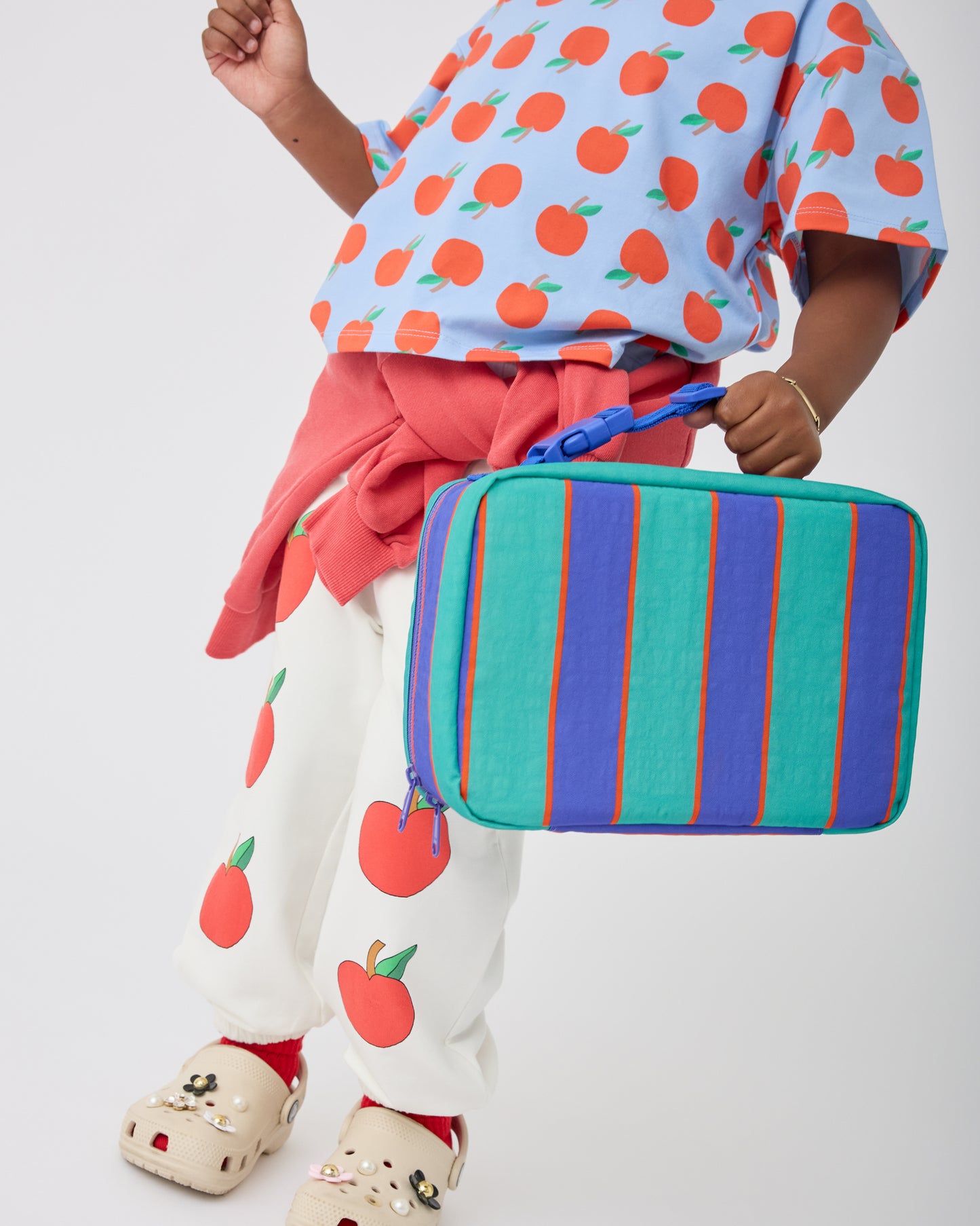 Child holding Cool Kid Lunch Box in Navy & Green Stripe, on a beige background.@model_info:Aliyana is 4 years old.