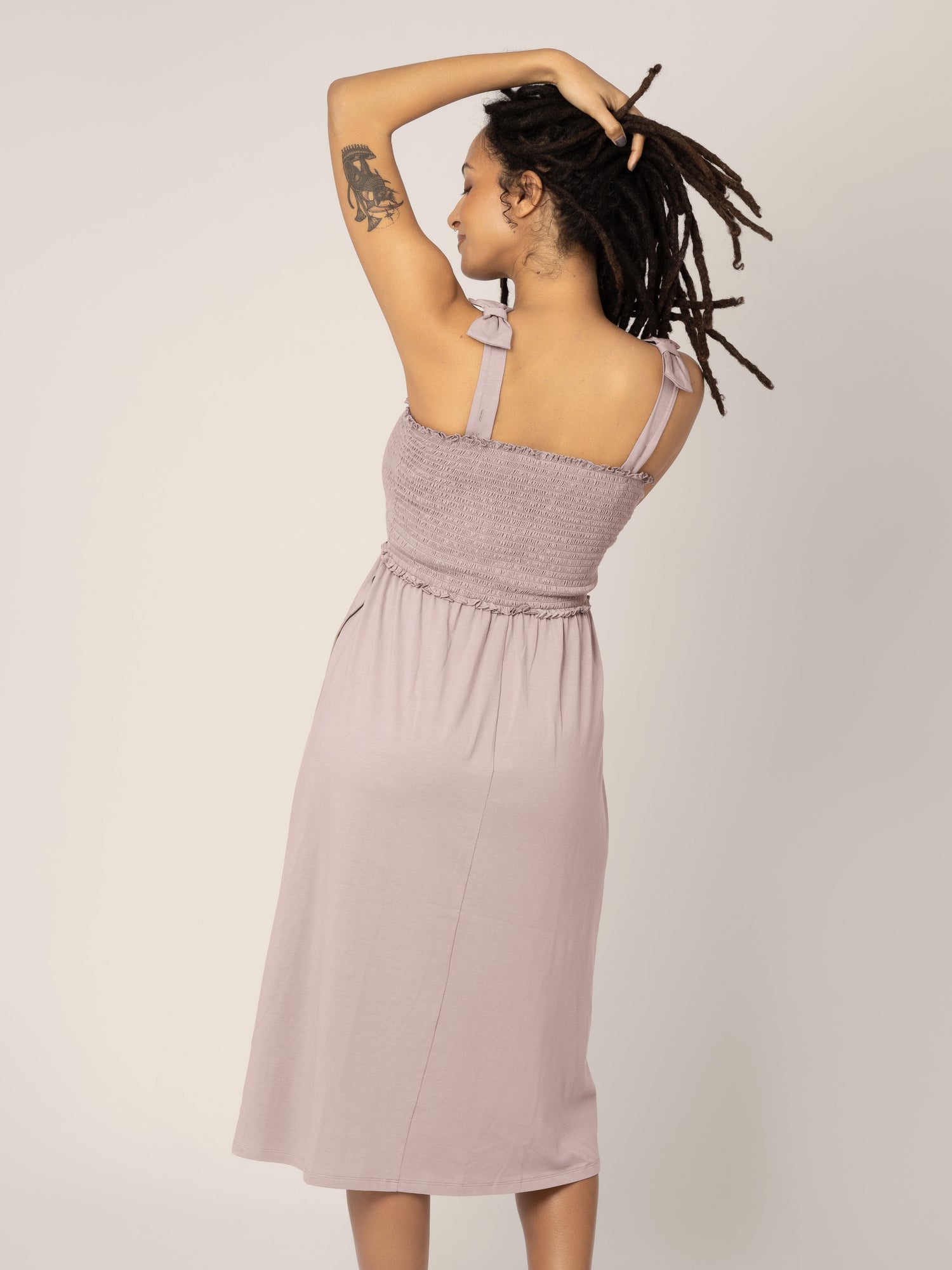 The back of a pregnant model wearing the Sienna Smocked Maternity & Nursing Dress in lilac stone