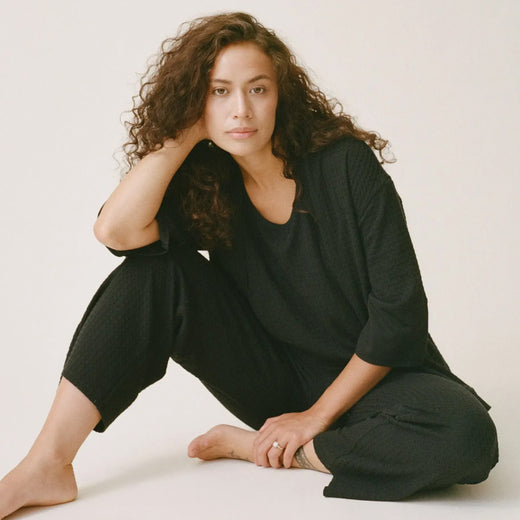Model is sitting on floor wearing Waffle Maternity & Nursing Three-Piece Lounge Set in Black on a beige background.