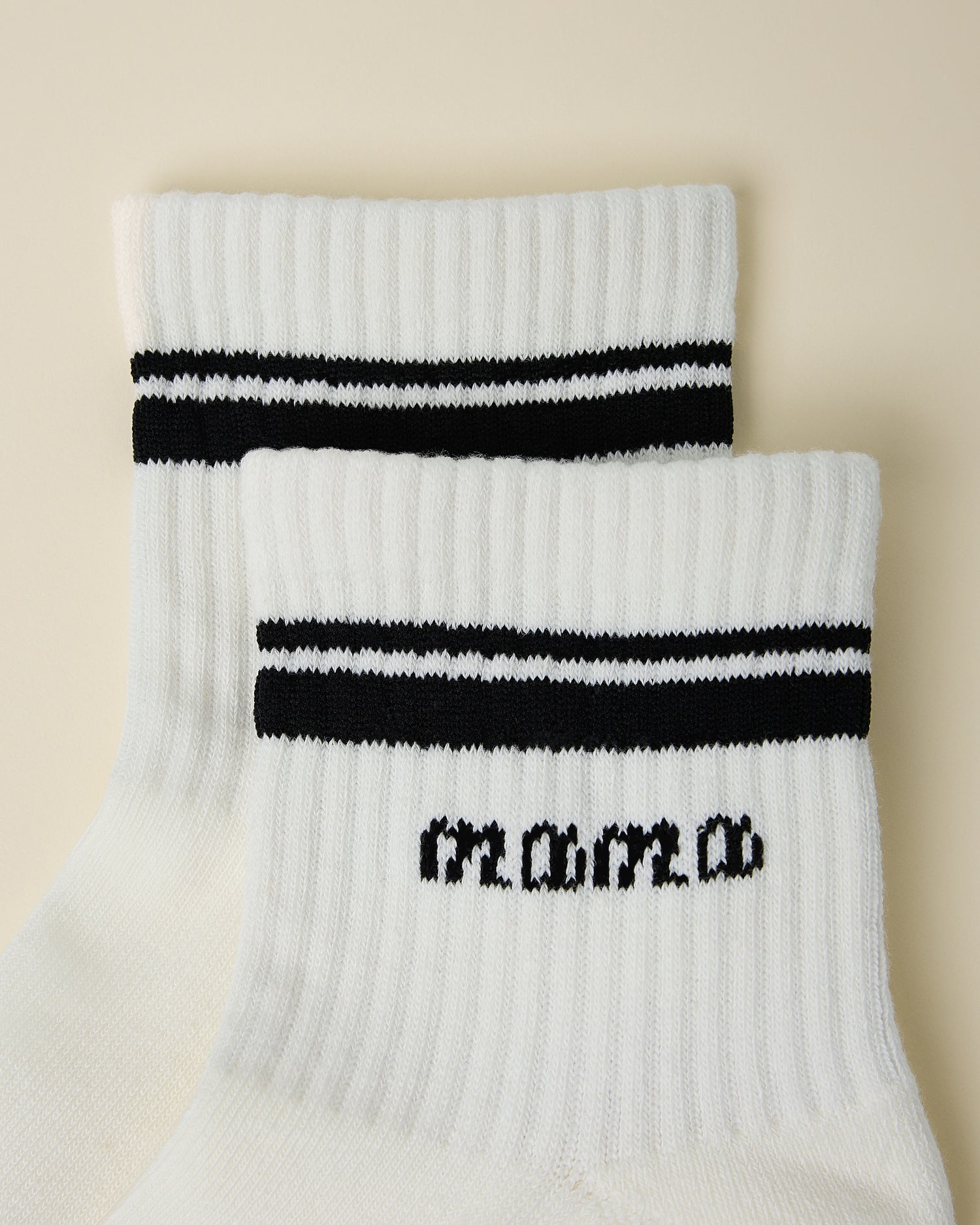 Close up of pair of Non-Slip Quarter Crew Socks in Ivory & Black on a beige background.