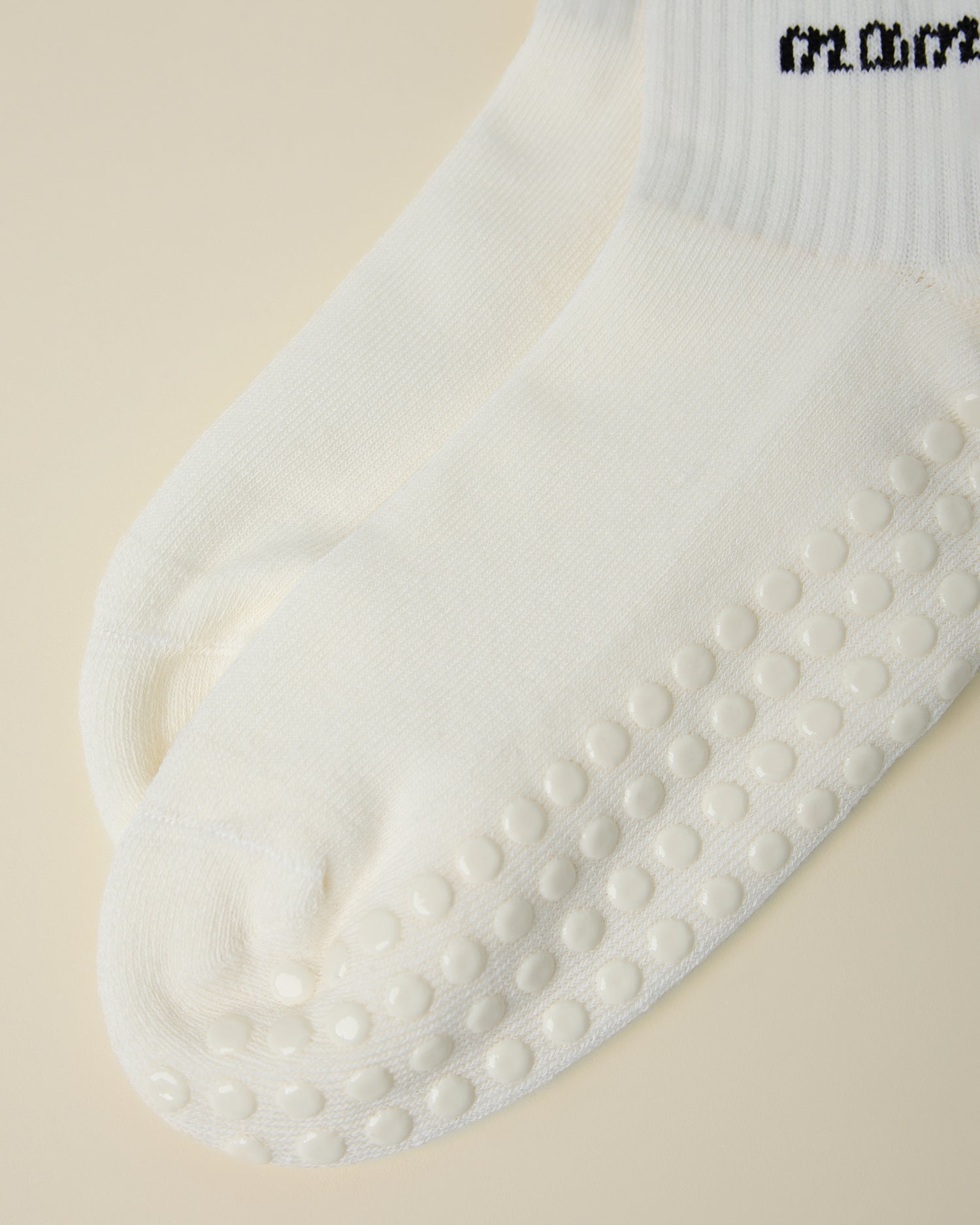 Close up of non-slip dots on a pair of Non-Slip Quarter Crew Socks in Ivory & Black on a beige background.