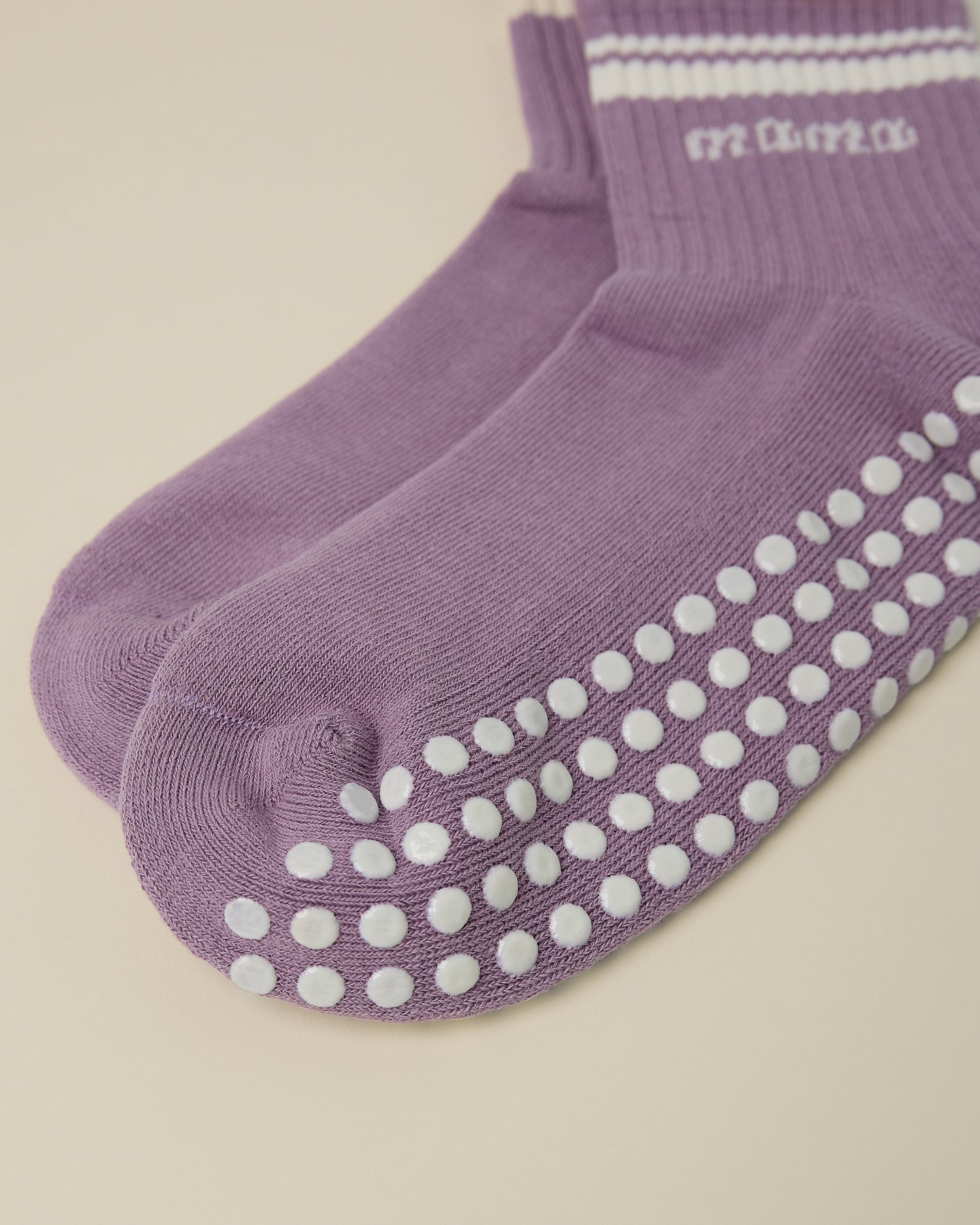 Close up of the non-slip dots on a pair of Non-Slip Quarter Crew Socks in Dusty Mauve & Ivory on a beige background.