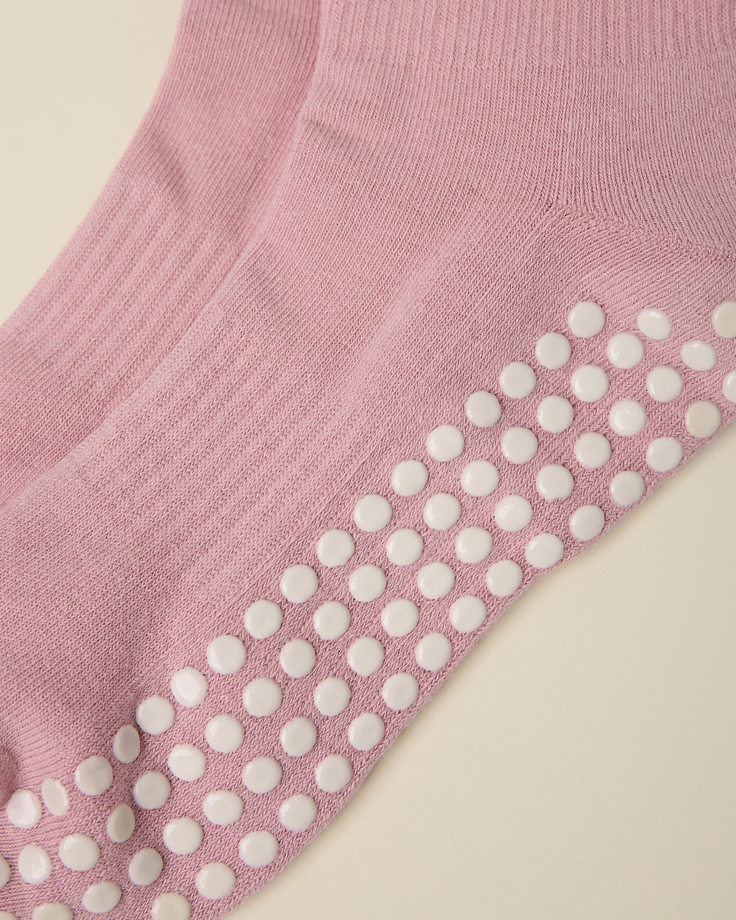 Close up of the white non-slip dots on a pair of Non-Slip Ruffle Ankle Socks in Light Mauve on a beige background
