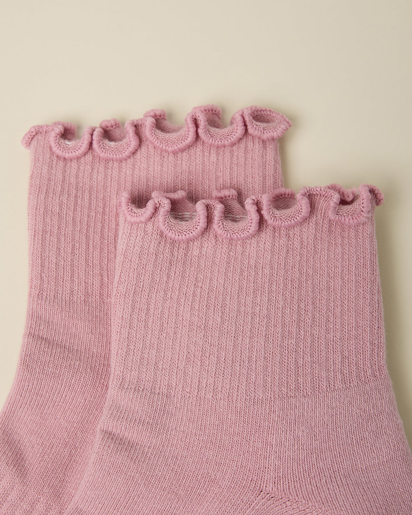 Close up of the ruffled cuff on a pair of Non-Slip Ruffle Ankle Socks in Light Mauve on a beige background