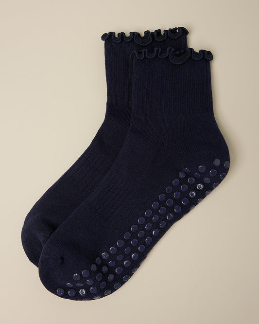 A pair of Non-Slip Ruffle Ankle Socks in Navy on a beige background.
