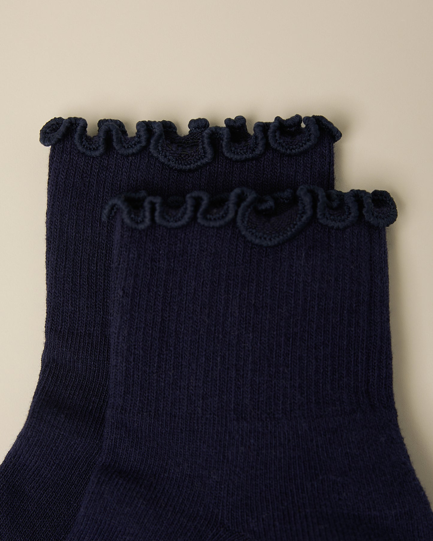 Close up of the ruffle on a pair of Non-Slip Ruffle Ankle Socks in Navy on a beige background.